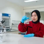 Teknisi laboratorium lingkungan wanita sedang melakukan analisis sampel cairan di laboratorium modern dengan peralatan pengujian profesional
